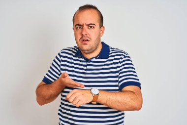 Izole beyaz arka plan üzerinde duran rahat çizgili polo giyen genç adam acele zaman izlemek için işaret, sabırsızlık, üzgün ve son gecikme için kızgın