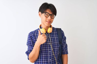 Izole beyaz arka plan üzerinde sırt çantası ve kulaklık giyen Çinli öğrenci adam el ile jest kadar mutlu başparmak yapıyor. Başarı göstererek kameraya bakan ifadeyi onaylama.