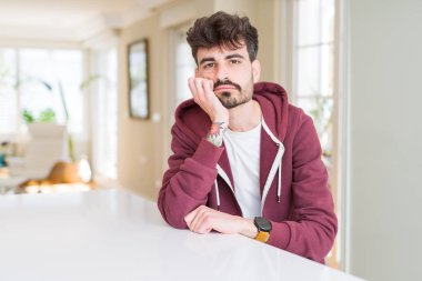 Beyaz düşünme yorgun ve bıkkın ile depresyon sorun çapraz kollar ile seyir tablo oturan rahat sweatshirt giyen genç adam.