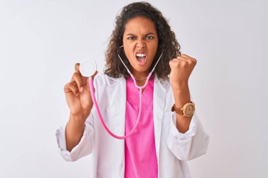 Genç Brezilyalı doktor kadın izole beyaz arka plan üzerinde duran stetoskop kullanarak kızgın ve öfke, deli ve yükseltilmiş el, öfke kavramı ile bağırarak sinirli