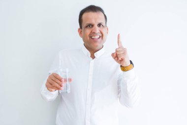 Orta yaş adam beyaz arka plan üzerinde bir bardak su içme mutlu yüz, bir numara ile bir fikir ya da soru işaret parmak ile şaşırttı