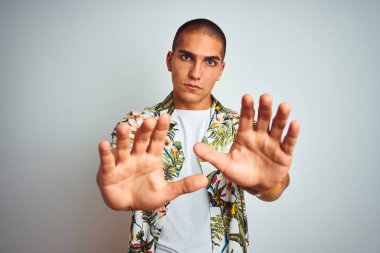 Tatilde beyaz arka plan üzerinde Hawaii gömleği giyen genç yakışıklı adam korku ve korku ifade ile korkmuş elleriyle jest durdurmak, şok içinde bağırarak. Panik kavramı.