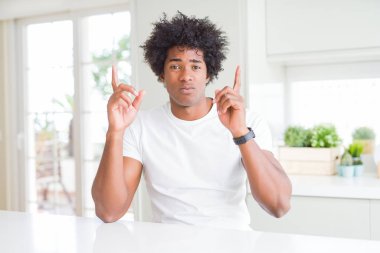 Evde oturan rahat beyaz tişört giyen genç Afro-Amerikan adam üzgün ve üzgün görünümlü, parmakları ile yön gösteren, mutsuz ve depresif.