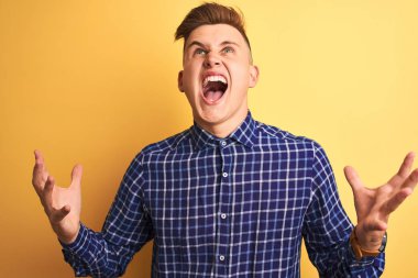 Genç yakışıklı adam izole sarı arka plan deli ve deli bağırarak ve agresif ifade ve kollar kaldırdı ile bağırıyor üzerinde duran rahat gömlek giyiyor. Hayal kırıklığı kavramı.