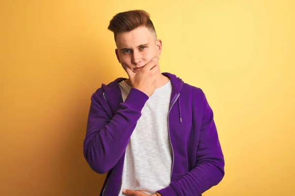 紫色のスウェットシャツを着た若いハンサムな男は 腕を組んで手を上げてカメラに自信を持って見て 孤立した黄色の背景の上に立っています ポジティブな考え方 — ストック写真