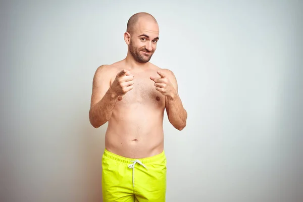 Young shirtless man on vacation wearing yellow swimwear over isolated background pointing fingers to camera with happy and funny face. Good energy and vibes.