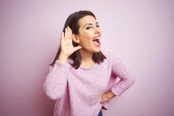 ピンクの孤立した背景の上にセーターを着ている若い美しいブルネットの女性は 噂やゴシップに耳を傾ける耳の上に笑顔 聴覚障害の概念 — ストック写真