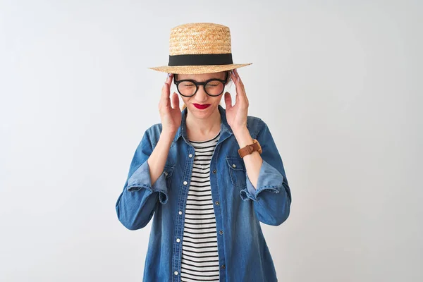 Redhead woman wearing denim shirt glasses and hat over isolated white background suffering from headache desperate and stressed because pain and migraine. Hands on head.