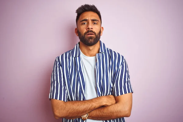 Young handsome indian man wearing summer striped shirt over isolated pink background skeptic and nervous, disapproving expression on face with crossed arms. Negative person.