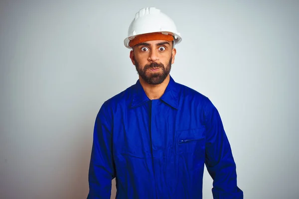 制服とヘルメットをかぶったハンサムなインド人労働者の男性は 白い背景の上に面白い顔で頬をふくらませます 空気で膨らんだ口 クレイジーな表情 — ストック写真