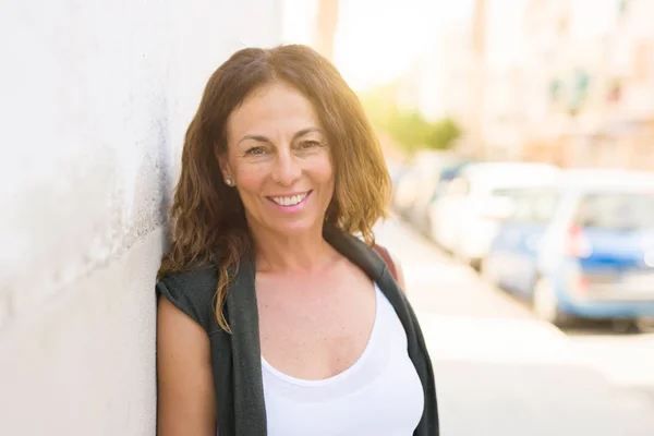 Beautiful middle age woman smiling cheerful leaning on a brick w — Stock Photo, Image