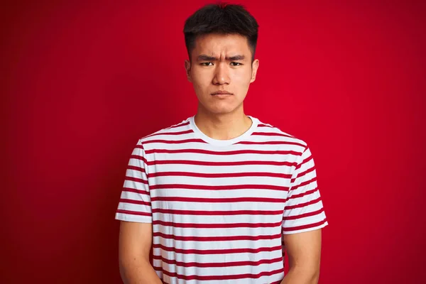 孤立した赤い背景に立つストライプのTシャツを着た若いアジア人の男性は 問題のために動揺して顔をしかめました 否定的な人 — ストック写真