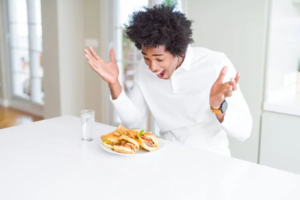 アフリカ系アメリカ人の空腹の男は クレイジーを祝う昼食のためにハンバーガーを食べて 腕を上げて 目を開けて興奮して成功に驚きました 勝者のコンセプト — ストック写真