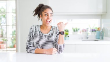 Afro saçlı güzel afro-amerikan kadın rahat çizgili kazak giyen mutlu yüz görünümlü ve başparmak ile yan işaret gülümseyerek.