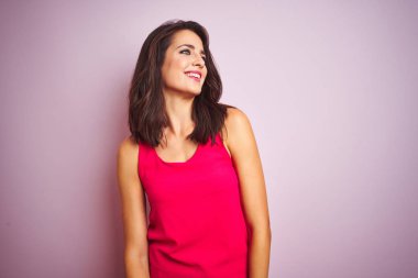 Pembe izole arka plan üzerinde duran t-shirt giyen genç güzel kadın yüzünde gülümseme, doğal ifade ile yan bakıyor. Gülmekten emin.