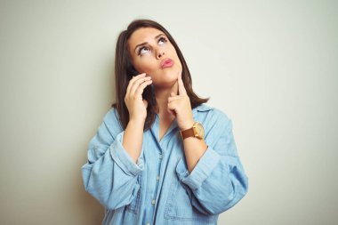 Genç güzel kadın izole arka plan üzerinde akıllı telefon kullanarak bir konuşma yapıyor ciddi yüz soru hakkında düşünme, çok karışık bir fikir