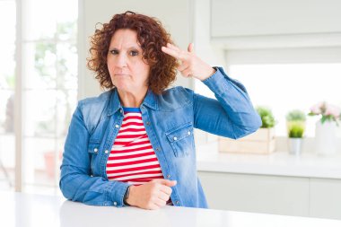 Evde kot ceket giyen kıvırcık saçlı orta yaş yaşlı kadın Çekim ve kendini silah gibi baş el ve parmaklarını gösteren öldürme, intihar jesti.