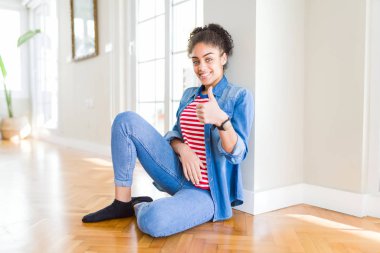 Hareketi el ile mutlu Yaşasın yapıyor katta oturan afro saçlı güzel genç Afro-Amerikan kadın. Kameraya bakarak başarı gösteren ile ifade onaylama.