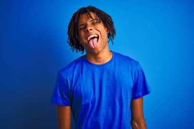 Afro amerikan adam dreadlocks giyen t-shirt izole mavi arka plan üzerinde duran komik ifade ile mutlu dil yapışmasını. Duygu kavramı.