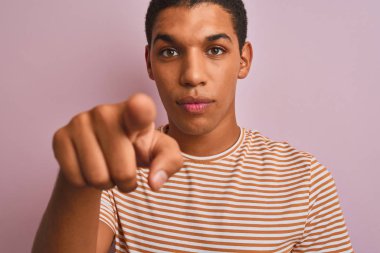 Genç yakışıklı arap adam kamera ve size parmak ile işaret izole pembe arka plan üzerinde duran çizgili t-shirt giyen, el işareti, önden olumlu ve kendinden emin jest