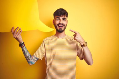 Dövme tutan konuşma balonu izole sarı arka plan üzerinde duran tutan genç adam çok mutlu el ve parmak ile işaret