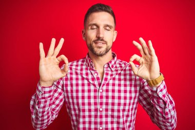 Kırmızı izole arka plan üzerinde Genç yakışıklı adam rahat ve gözleri parmakları ile meditasyon jest yapıyor kapalı gülümseyerek. Yoga konsepti.