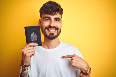 Kendine işaret sürpriz yüzü ile izole sarı arka plan üzerinde Kanada Kanada pasaportu giyen dövme ile genç adam