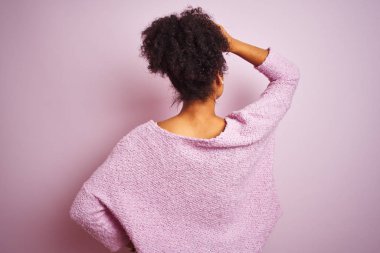 Genç afro-amerikan kadın kış kazak giyen izole pembe arka plan üzerinde duran geriye başında el ile şüphe düşünme