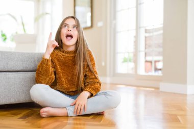 Güzel genç kız çocuk evde yerde oturan başarılı bir fikir ile parmak işaret. Çıktı ve mutlu. Bir numara.