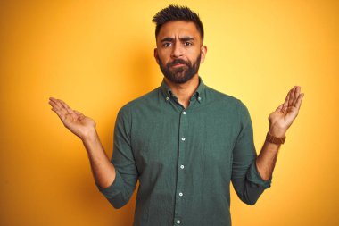 Genç Hintli işadamı zarif gömlek giyen izole beyaz arka plan üzerinde duran habersiz ve kolları ve elleri ile karışık ifade kaldırdı. Şüphe kavramı.