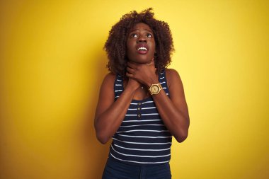 Genç Afrikalı afro kadın izole sarı arka plan üzerinde çizgili t-shirt giyen bağırarak ve boğulma çünkü acı boğmak. Sağlık sorunu. Boğulma ve intihar kavramı.