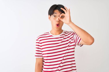 Gözlük takan ve çizgili tişört giyen genç adam izole beyaz arka plan üzerinde duran ok jesti yaparak şaşkın bir yüz, göz parmaklarıile bakarak şok etti. İnanmayan ifade.