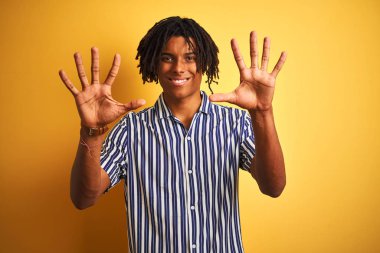 Dreadlocks izole sarı arka plan üzerinde rahat çizgili t-shirt giyen Afro adam gösteren ve emin ve mutlu gülümserken parmakları on numara ile işaret.