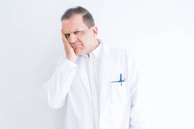 Orta yaş doktor adam beyaz arka plan üzerinde tıbbi ceket giyen yorgun görünümlü ve çapraz kollar ile depresyon sorunları ile sıkılmış düşünme.
