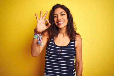 Genç güzel kadın çizgili t-shirt izole sarı arka plan üzerinde duran giyen olumlu el ve parmakları ile ok işareti yapıyor gülümseyerek. Başarılı ifade.