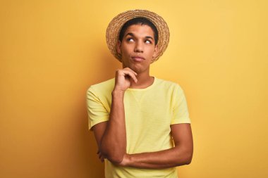 Genç yakışıklı Arap adam t-shirt ve yazlık şapka giyen izole yelllow arka plan çene üzerinde soru, dalgın ifade düşünme el ile. Düşünceli bir yüzle gülümsüyor. Şüphe kavramı.