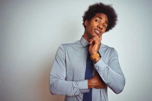 American business man with afro hair wearing shirt and tie over isolated white background with hand on chin thinking about question, pensive expression. Smiling with thoughtful face. Doubt concept.