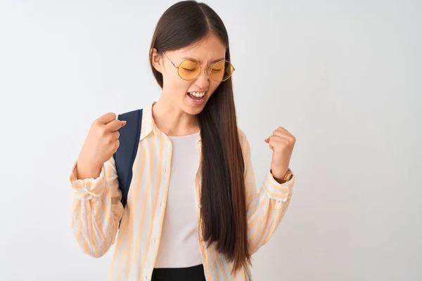 孤立した白い背景の上にメガネとバックパックを身に着けている若い中国人学生の女性は 腕を上げ 笑顔で成功のために叫んで勝者のジェスチャーをして非常に幸せで興奮しています お祝いのコンセプト — ストック写真