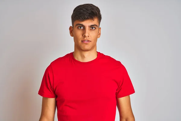 赤いTシャツを着た若いインド人男性が 真剣な表情で孤立した白い背景の上に立っている カメラを見てシンプルで自然な — ストック写真