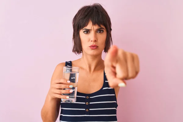 年轻的美丽的女人拿着一杯水站在孤立的粉红色背景 用手指指着相机和你 手标志 积极和自信的姿态从前面 — 图库照片