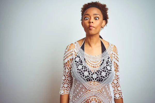 Young african american woman with afro hair wearing a bikini over white isolated background making fish face with lips, crazy and comical gesture. Funny expression.