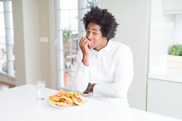 昼食にハンバーガーを食べるアフリカ系アメリカ人の男は 口を噛む爪に手を当て ストレスと緊張を見ています 不安の問題 — ストック写真