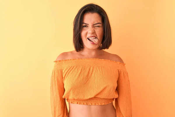 カジュアルなTシャツを着た若い美しい女性は 面白い表情で舌を突き出して孤立したオレンジ色の背景の上に立っています 感情の概念 — ストック写真