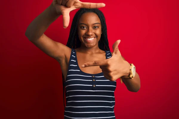 縞模様のTシャツを着た若いアフリカ系アメリカ人女性が 赤い背景に孤立した笑顔で立っており 手や指で幸せな顔をしている 創造性と写真の概念 — ストック写真