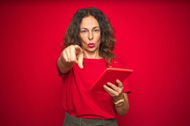 Orta yaş yaşlı kadın kırmızı izole arka plan üzerinde touchpad tablet kullanarak kamera ve size parmak ile işaret, el işareti, önden olumlu ve kendinden emin jest