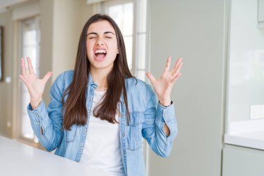 Güzel genç kadın evde beyaz masada oturan deli ve öfkeli çığlık ve saldırgan ifade ve kollar ile bağırarak kaldırdı. Hayal kırıklığı kavramı.