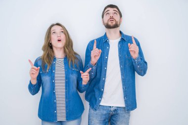 Genç güzel çift beyaz izole arka plan üzerinde birlikte ayakta şaşırmış ve baktı ve parmakları ile işaret ve kolları kaldırdı şaşırttı.