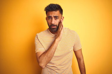 Genç hint adam ağız üzerinde izole sarı arka plan el üzerinde duran t-shirt giyen gizli söylenti söylüyorum, kötü niyetli konuşma konuşma fısıldıyor