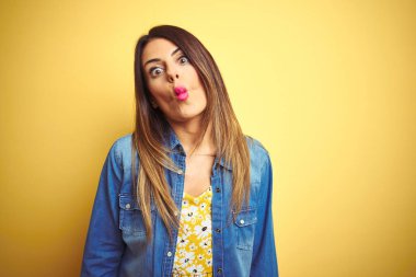 Genç güzel kadın dudakları, deli ve komik jest ile balık yüz yapma sarı izole arka plan üzerinde duran. Komik ifade.