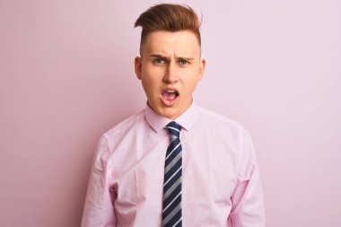 Genç yakışıklı işadamı gömlek ve kravat şok karşısında izole pembe arka plan üzerinde duran, şüpheci ve alaycı görünümlü, açık ağız ile şaşırttı
